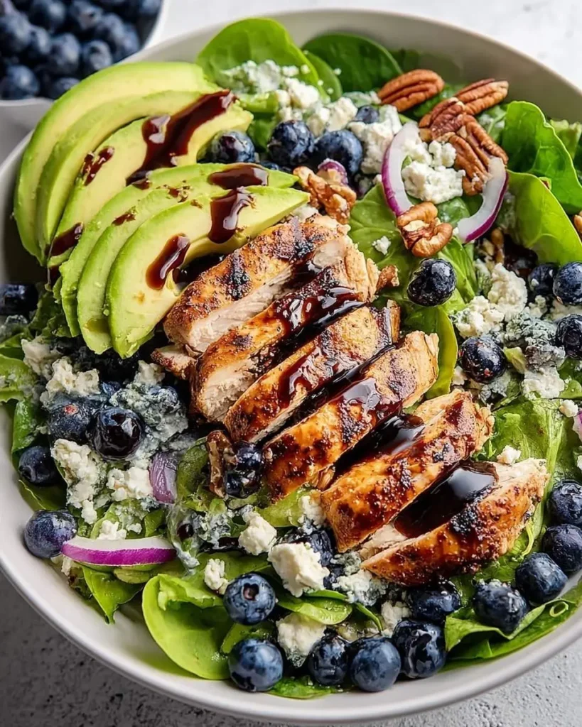 A vibrant Chicken Blueberry Feta Salad in a white bowl, featuring grilled chicken, blueberries, feta, avocado, pecans, and balsamic glaze.