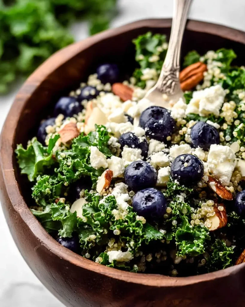 A close-up of a Kale Blueberry Quinoa Salad with feta and almonds in a rustic wooden bowl with a fork.