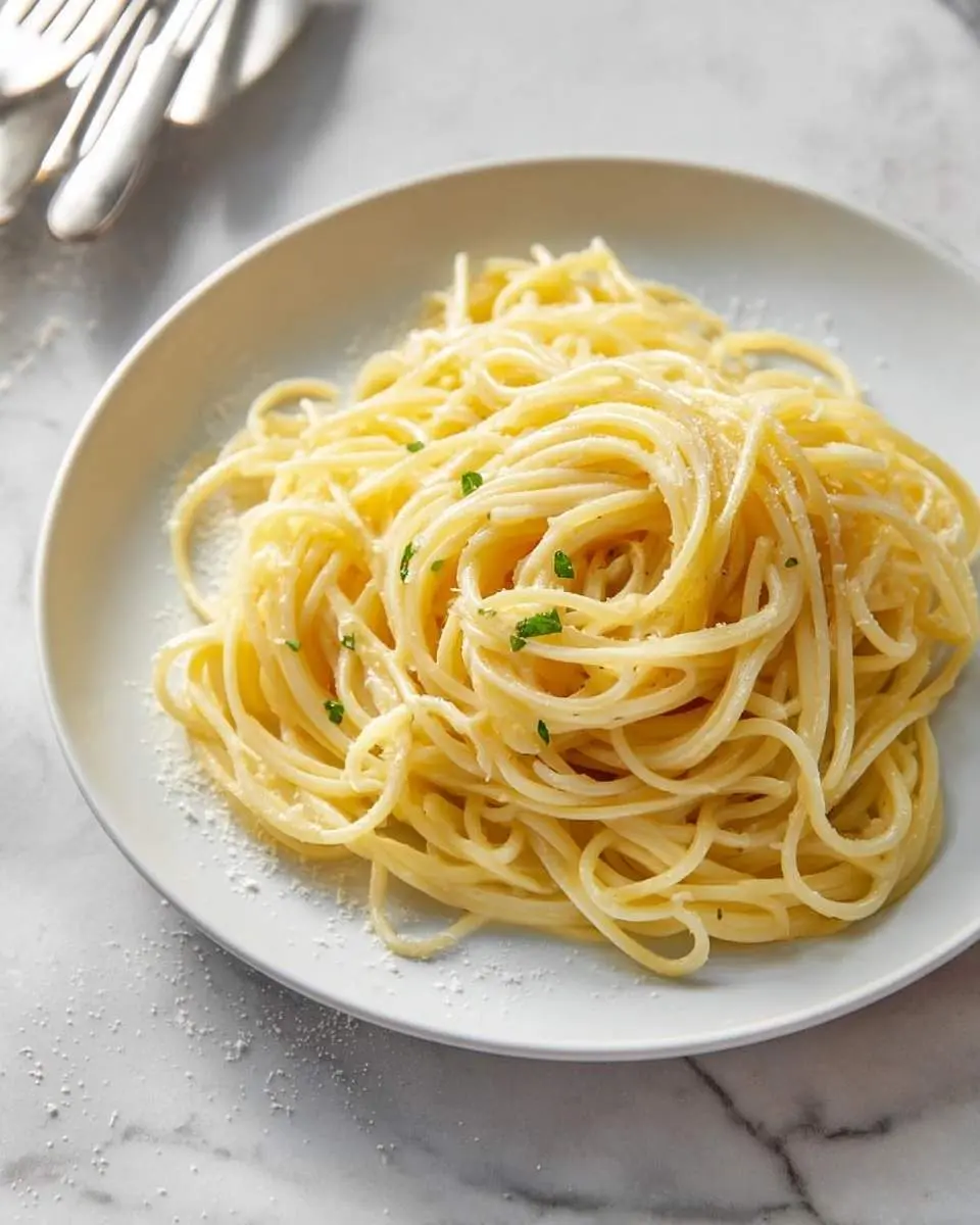 A plate of perfectly cooked butter noodles, lightly coated in sauce, garnished with parsley and grated cheese on a marble surface.