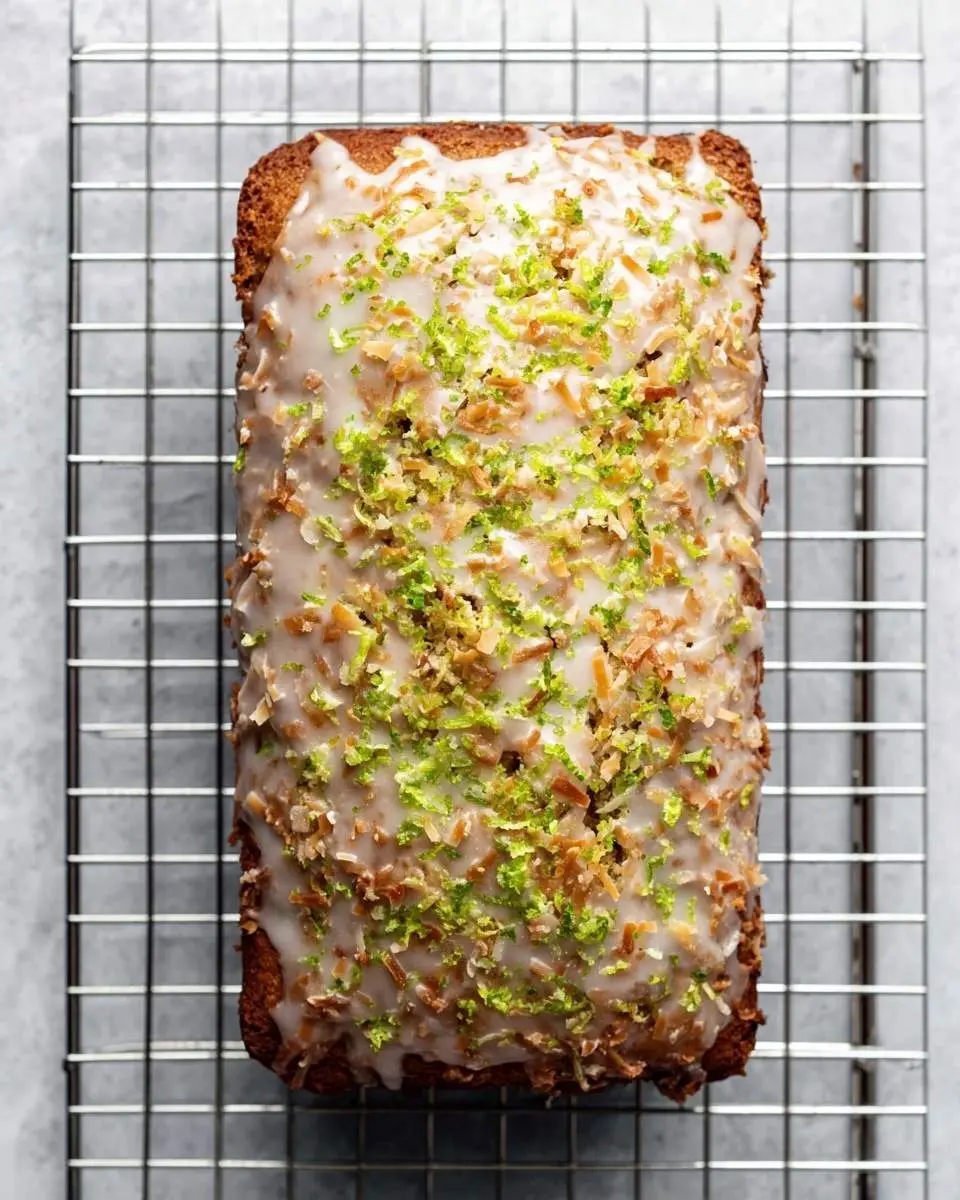 Coconut Lime Glazed Banana Bread 2 A delicious loaf of Coconut Lime Glazed Banana Bread on a cooling rack, topped with white icing, lime zest, and toasted coconut.