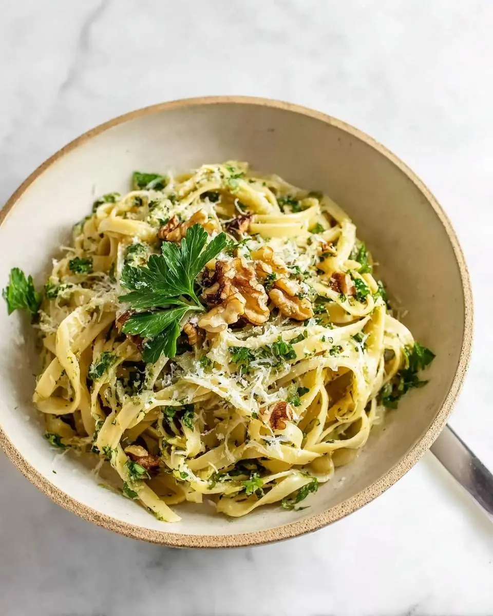 A ceramic bowl filled with creamy Fettuccine with Walnuts and Parsley, garnished with grated Parmesan cheese and fresh herbs.