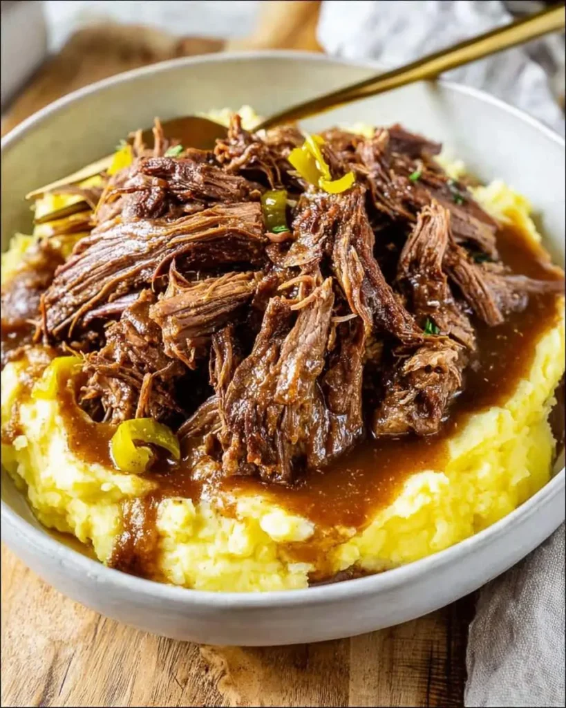 A hearty bowl of tender Mississippi Pot Roast, shredded and served over creamy mashed potatoes with rich gravy and pepper slices.