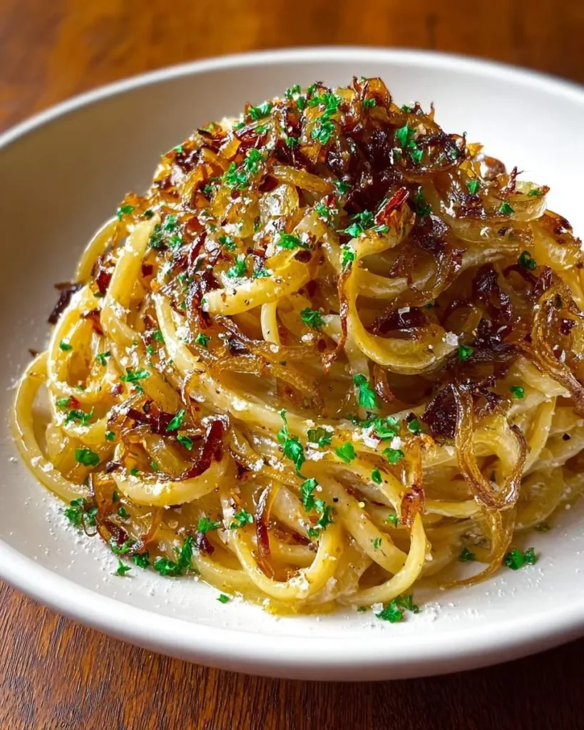 A close-up of a white bowl filled with spaghetti generously topped with glistening caramelised onion pasta and fresh parsley.
