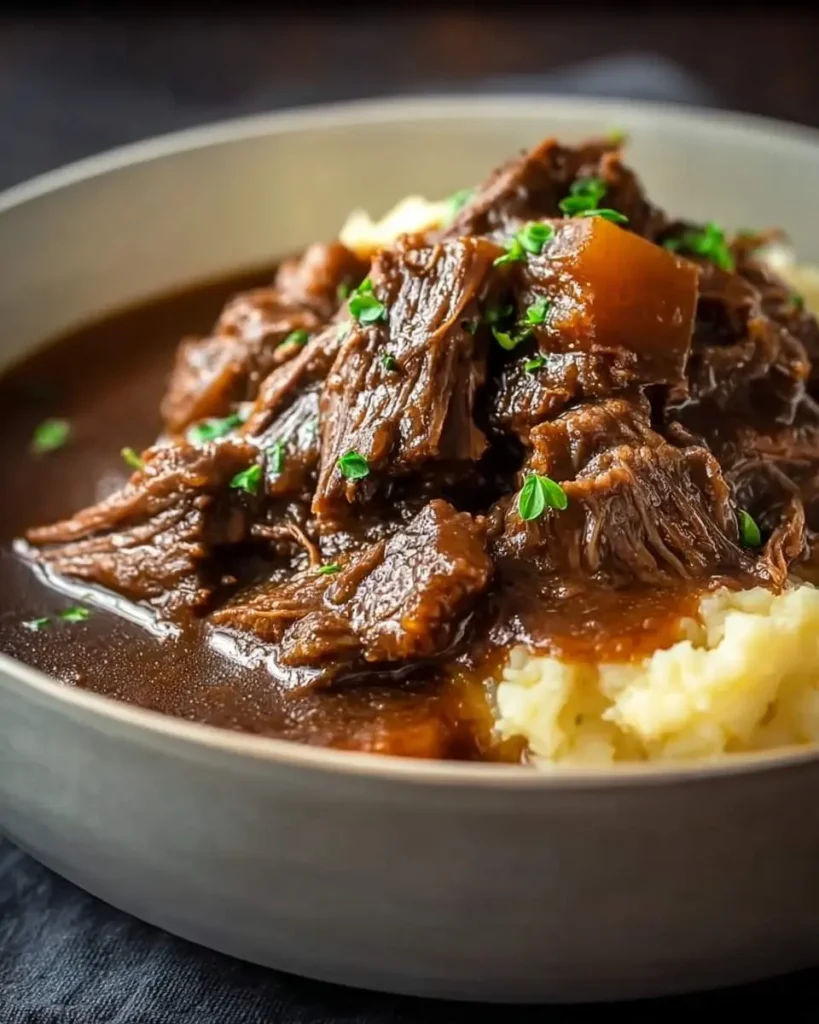 A hearty bowl of tender Slow Cooker Beef Manhattan served over creamy mashed potatoes and garnished with fresh herbs.