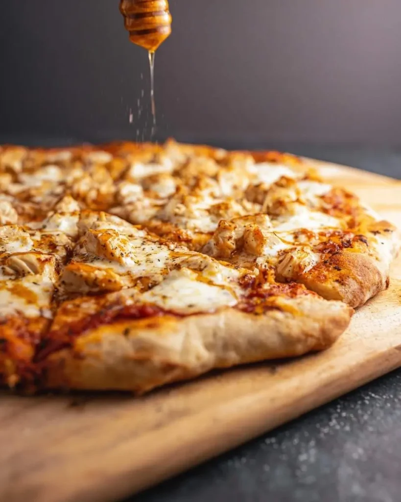 A delicious hot honey pizza with grilled chicken and melted cheese, being drizzled with golden honey from a wooden dipper.