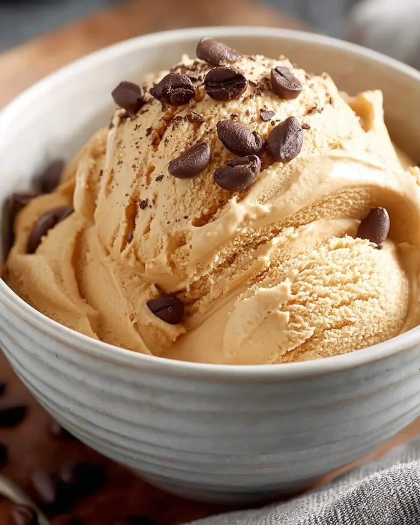 Close-up of creamy Ninja Creami Coffee Ice Cream in a white bowl, garnished with whole coffee beans and chocolate sprinkles.