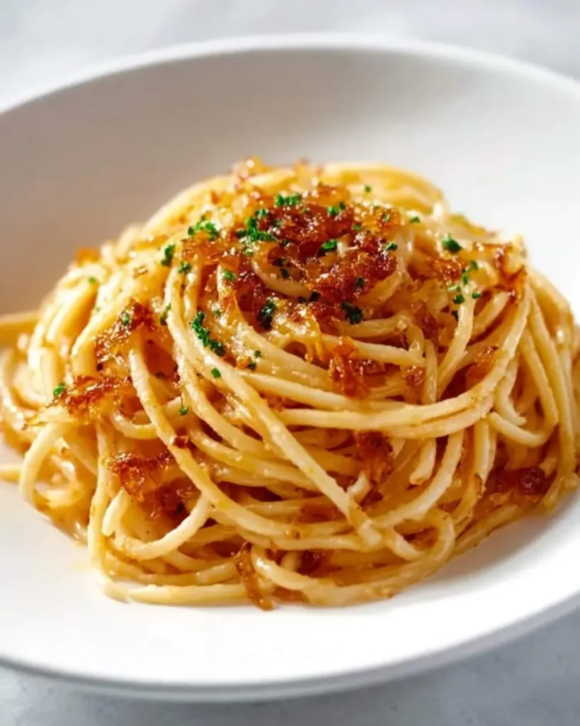 A close-up shot of a white bowl brimming with golden Caramelized Shallot Pasta, garnished with chopped fresh chives.