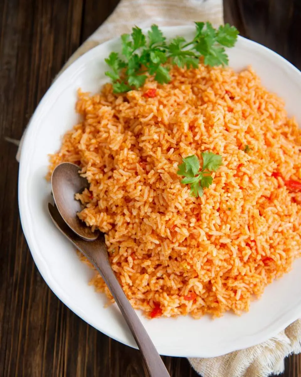 Mexican Rice 1 A white serving dish filled with vibrant orange Mexican Rice, garnished with fresh cilantro, and a wooden spoon.