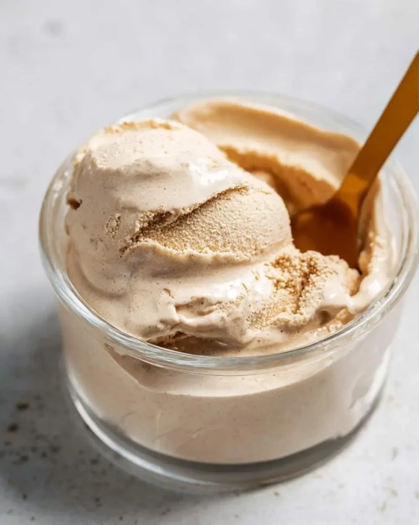 A clear glass bowl filled with creamy scoops of homemade Ninja Creami Cinnamon Ice Cream, featuring a gold spoon.
