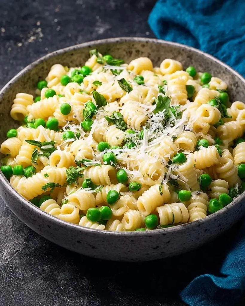 A close-up of a delicious Pasta and Peas Recipe served in a speckled grey bowl, garnished with fresh mint and grated Parmesan cheese.