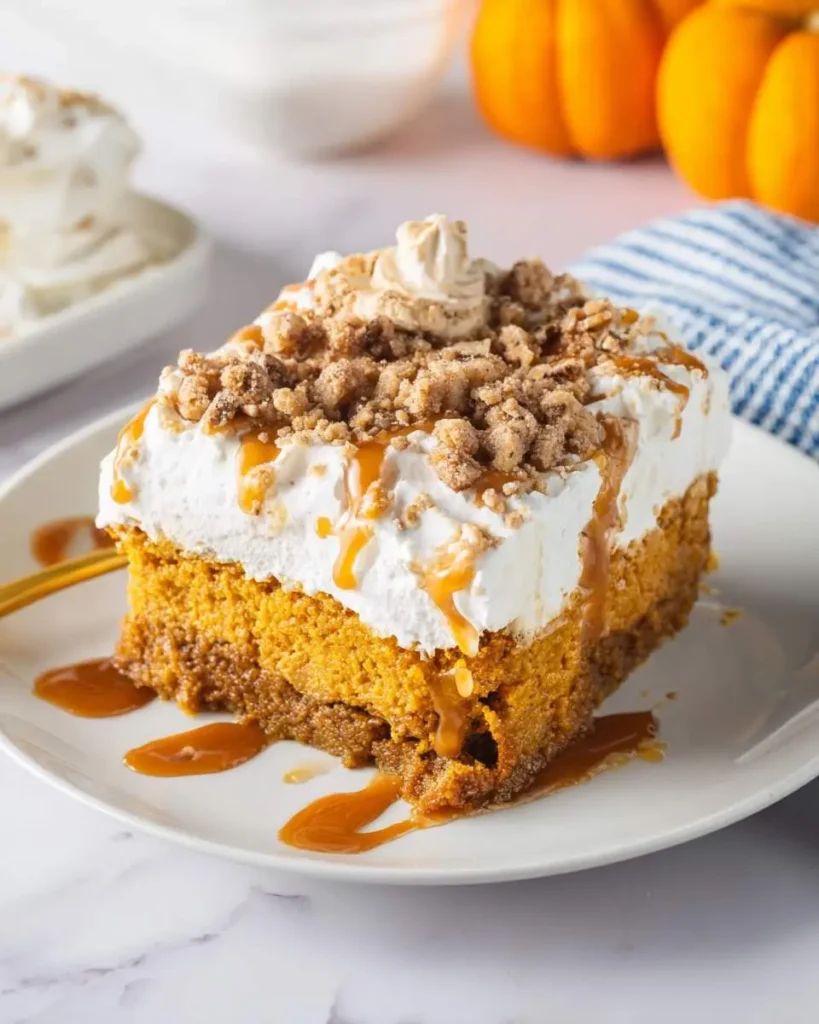 A delicious slice of pumpkin poke cake topped with whipped cream, caramel drizzle, and a crunchy streusel crumble.