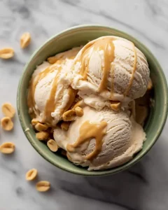 Three scoops of peanut butter banana ice cream in a green bowl topped with peanut butter drizzle and chopped peanuts.