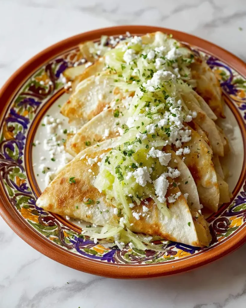 Golden crispy Potato Quesadillas topped with fresh lettuce, crumbled cheese, and herbs on a colorful Mexican plate.