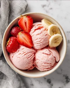 Three scoops of creamy Strawberry Banana Ice Cream topped with fresh strawberries and banana slices in a bowl.