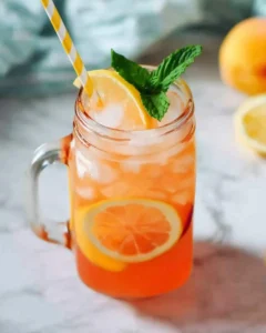 Refreshing peach lemonade served in a mason jar with ice, lemon slices, mint, and a striped straw.