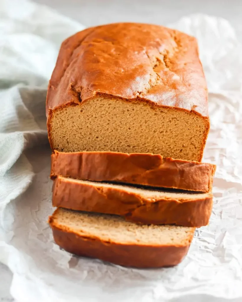 A freshly baked loaf of peanut butter bread with three slices cut and stacked in front, resting on parchment paper.