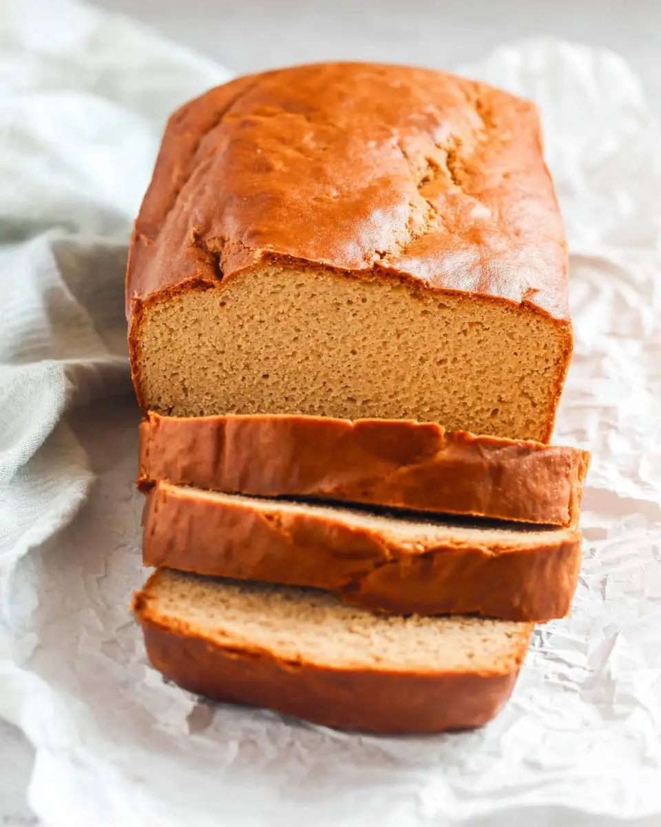 Peanut Butter Bread 4 A freshly baked loaf of peanut butter bread with three slices cut and stacked in front, resting on parchment paper.