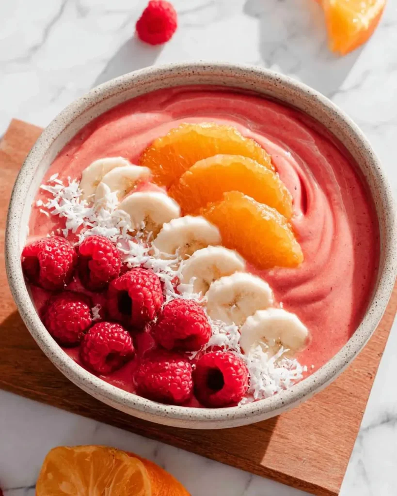 Raspberry Orange Smoothies Recipes Bowl topped with fresh banana slices, orange segments, raspberries, and coconut flakes.